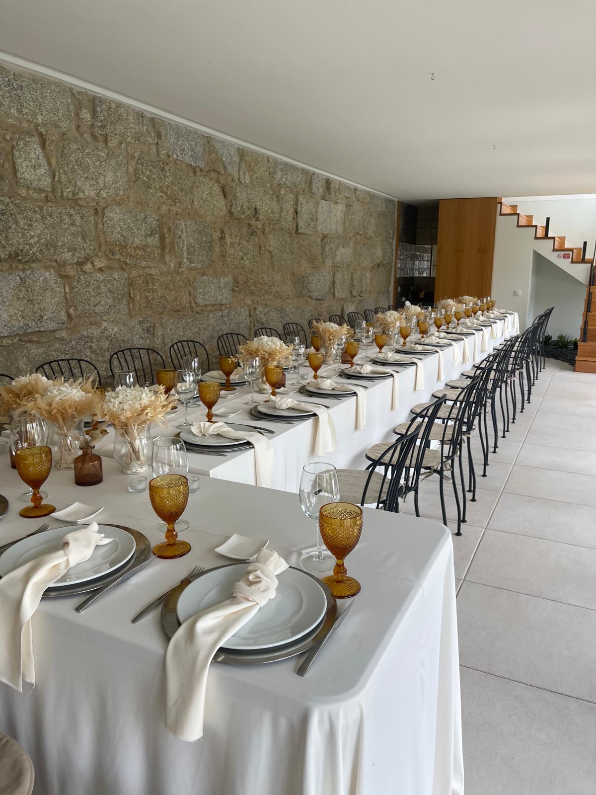 Mesa comprida com toalha branca e lugares preparados para uma celebração